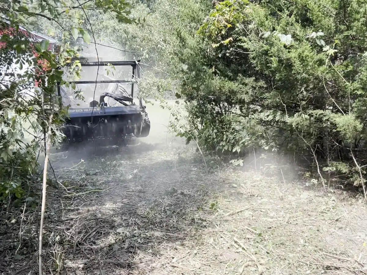 Forestry mulcher opening a lane near a red barn