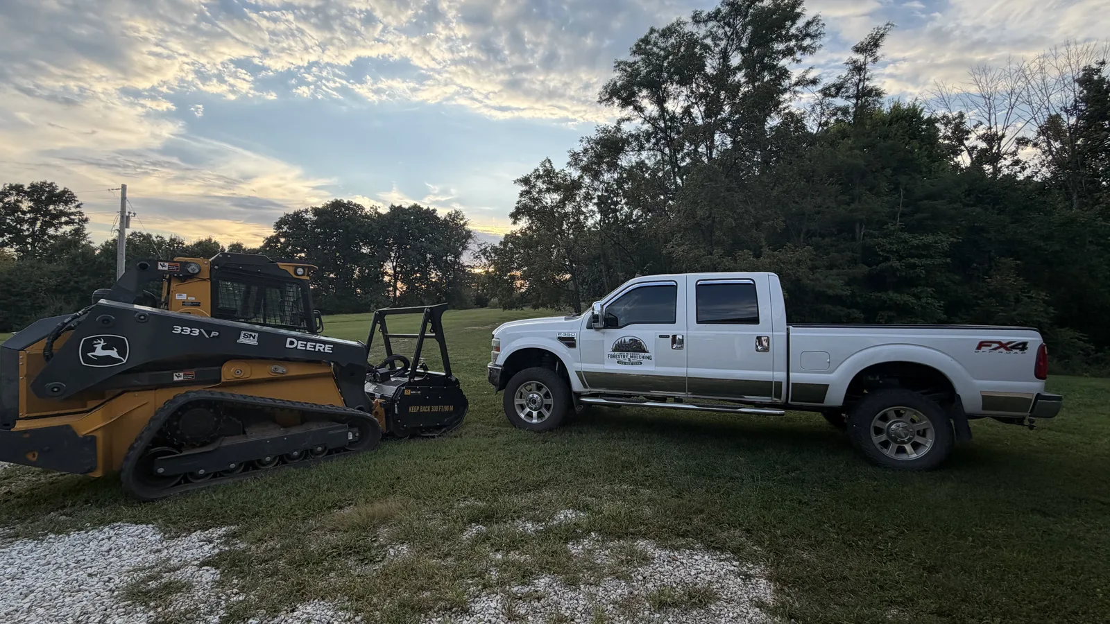 Company pickup and forestry mulcher on a mown field in the evening