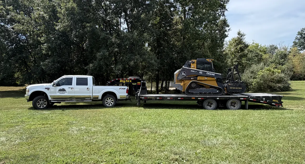 Wide view of the company truck, gooseneck trailer and forestry mulcher on a mown field